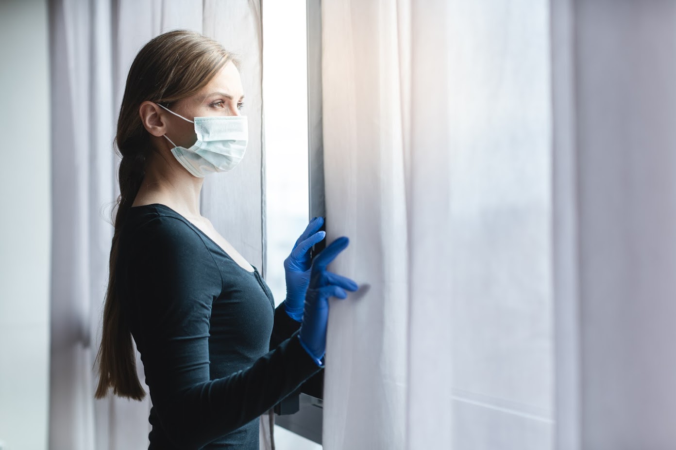 Bored woman in corona quarantine looking out of window to the street