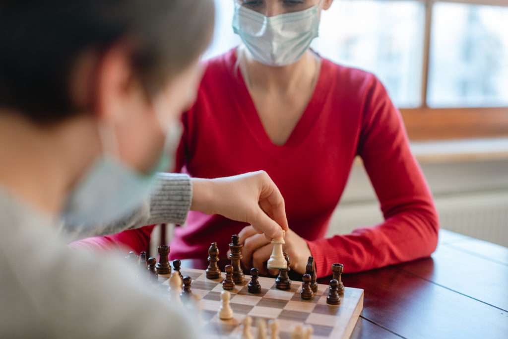 Famile trägt Masken in der Covid-19 Krise und spielt daheim Schach